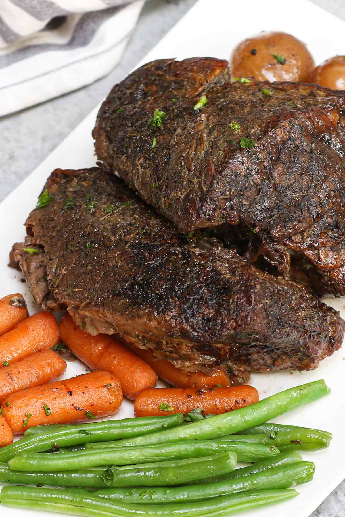 A slow cooked top round roast on a serving platter with vegetables