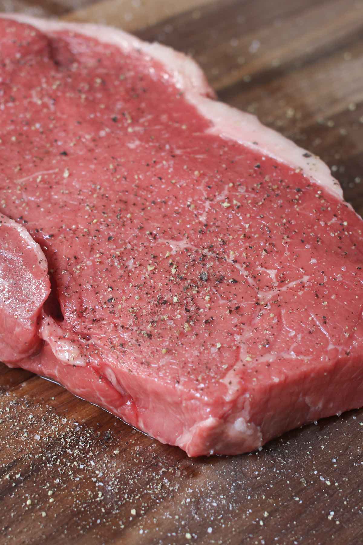 Closeup of a raw top sirloin steak cut one inch thick and seasoned with salt and pepper.