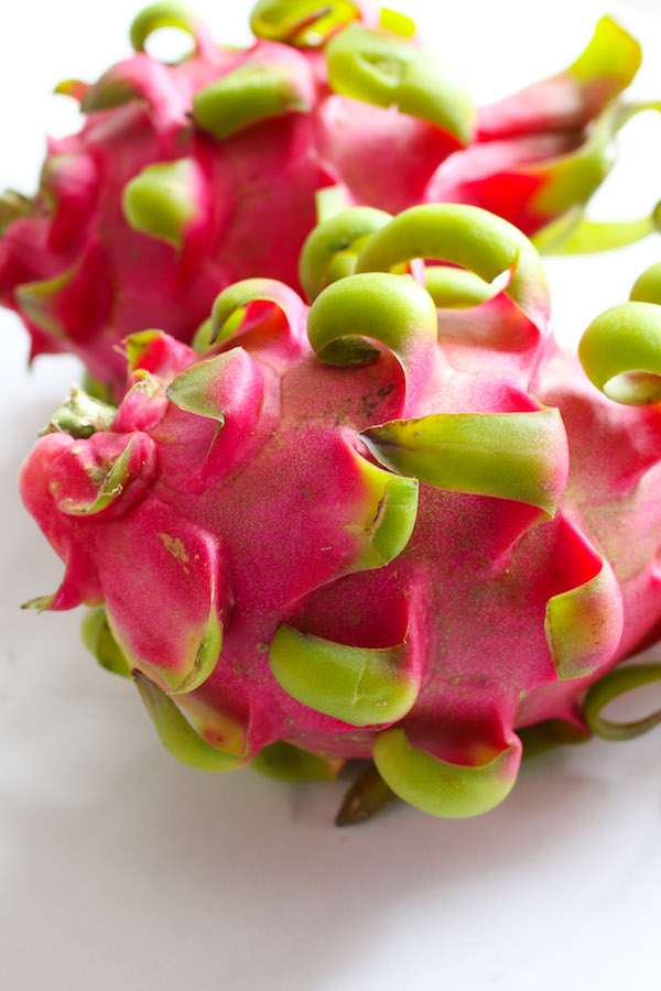 Closeup of two whole pink dragon fruits at the peak of ripeness with some minor blemishes which are normal for this tropical fruit