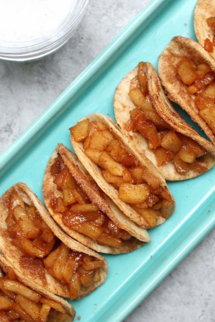 Serving platter full of apple pie tacos showing the crispy taco shells and soft apple filling inside