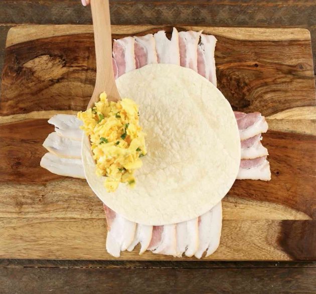 Photo os assembling a Bacon covered Crunchwrap with scrambled eggs and cheese inside
