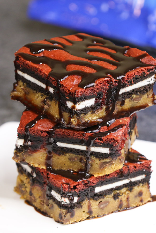 A stack of decadent red velvet slutty brownies on a plate with chocolate sauce drizzled on top