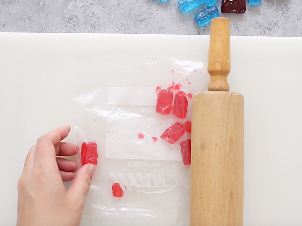 Crushing Jolly Rancher candies in a zip-lock bag using a rolling pin.