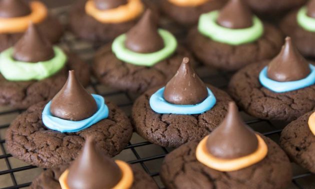 Witch hat cookies on a wire rack with different colors of frosting attaching the Hershey's kisses on top